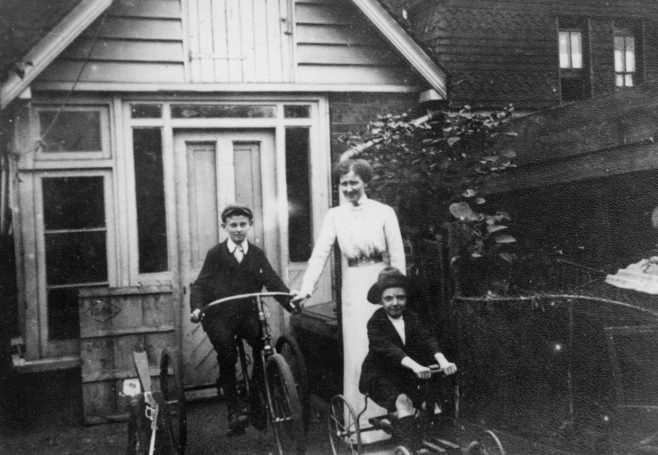 An early picture of John shows him aboard his first mode of transport, a large and rather splendid tricycle, shown here in the back garden at Merle Cottage with his brother Reg and their mother Alice. 